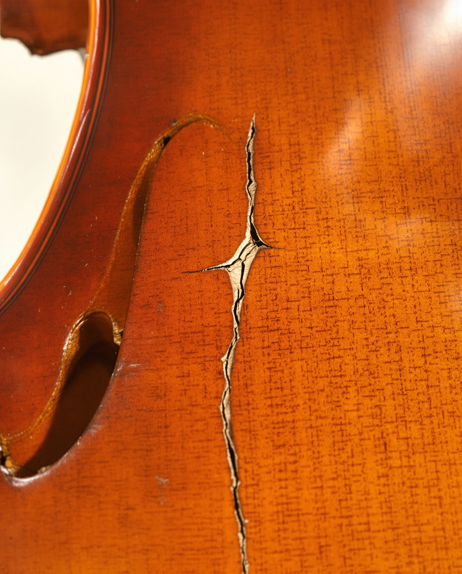 Gros plan sur la table d'harmonie d'un violoncelle ancien. L'image met en évidence une fine fissure près du pied du chevalet, ainsi que l'usure naturelle du vernis, illustrant les signes de vieillesse à surveiller.