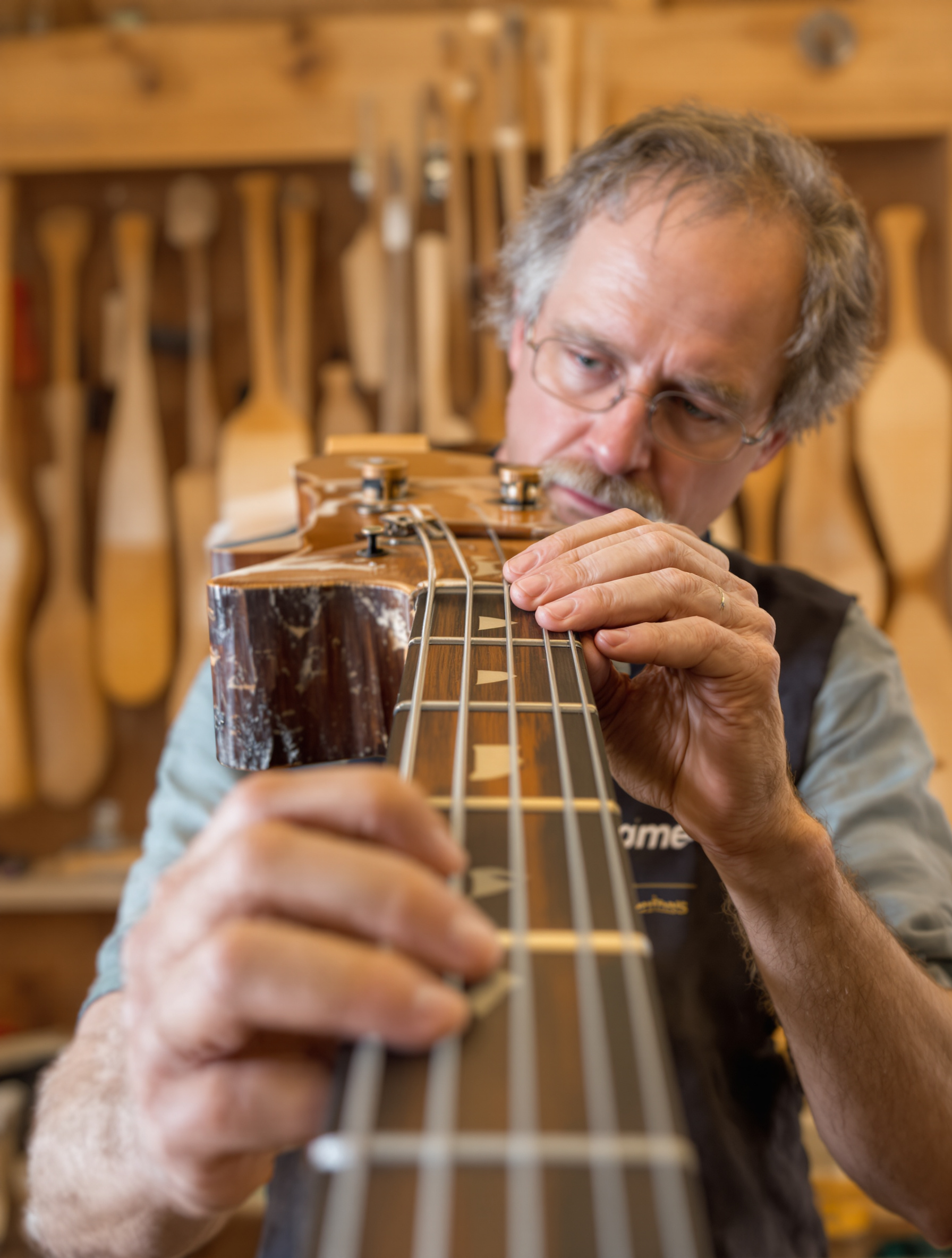 Inspection experte du manche d'une guitare basse par un luthier.