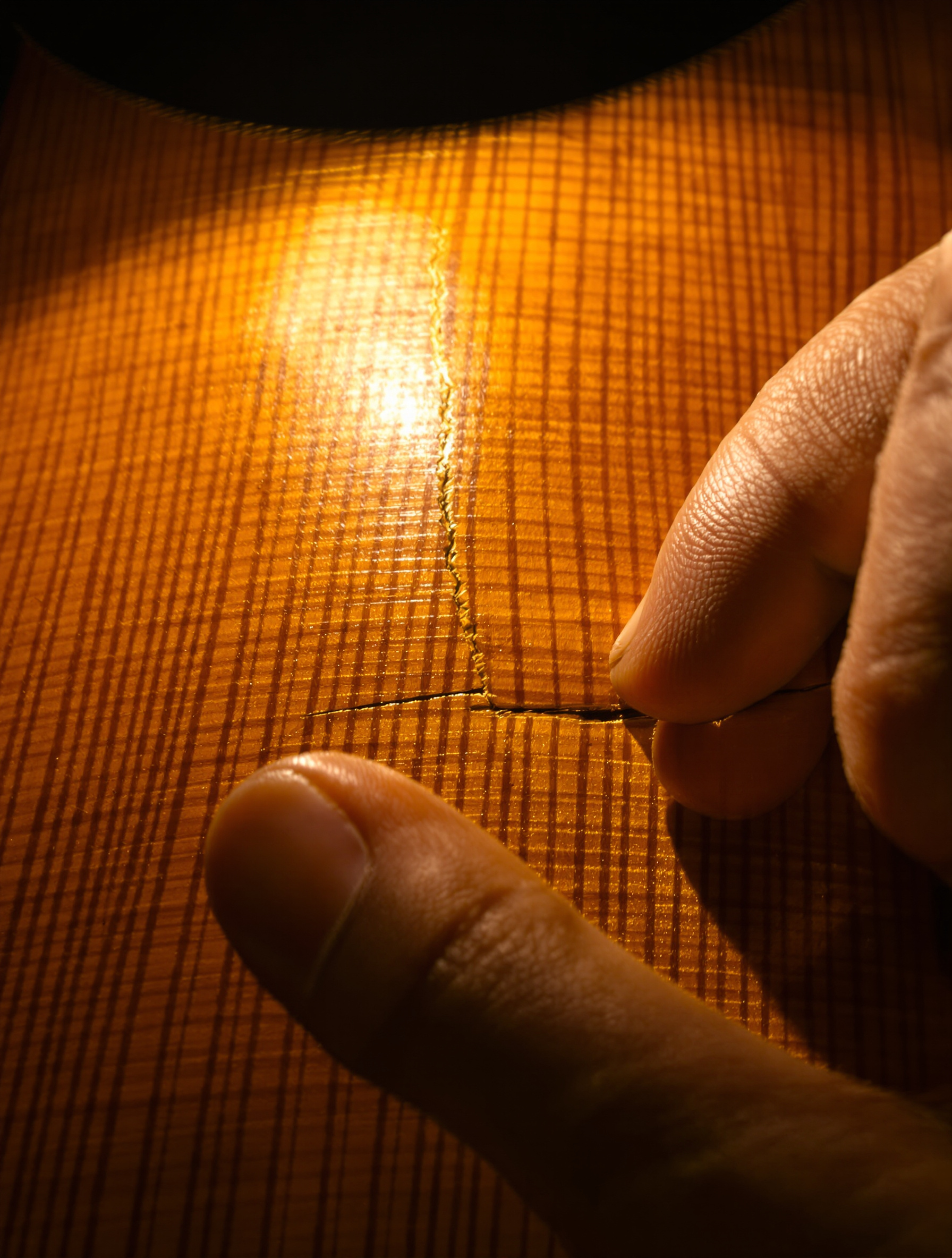 Inspection d’un violon sous une lumière rasante mettant en évidence une fissure parallèle au fil du bois.
